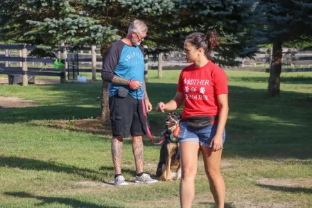 A dog trainer explaining something to a student, with another student and their dog in the background